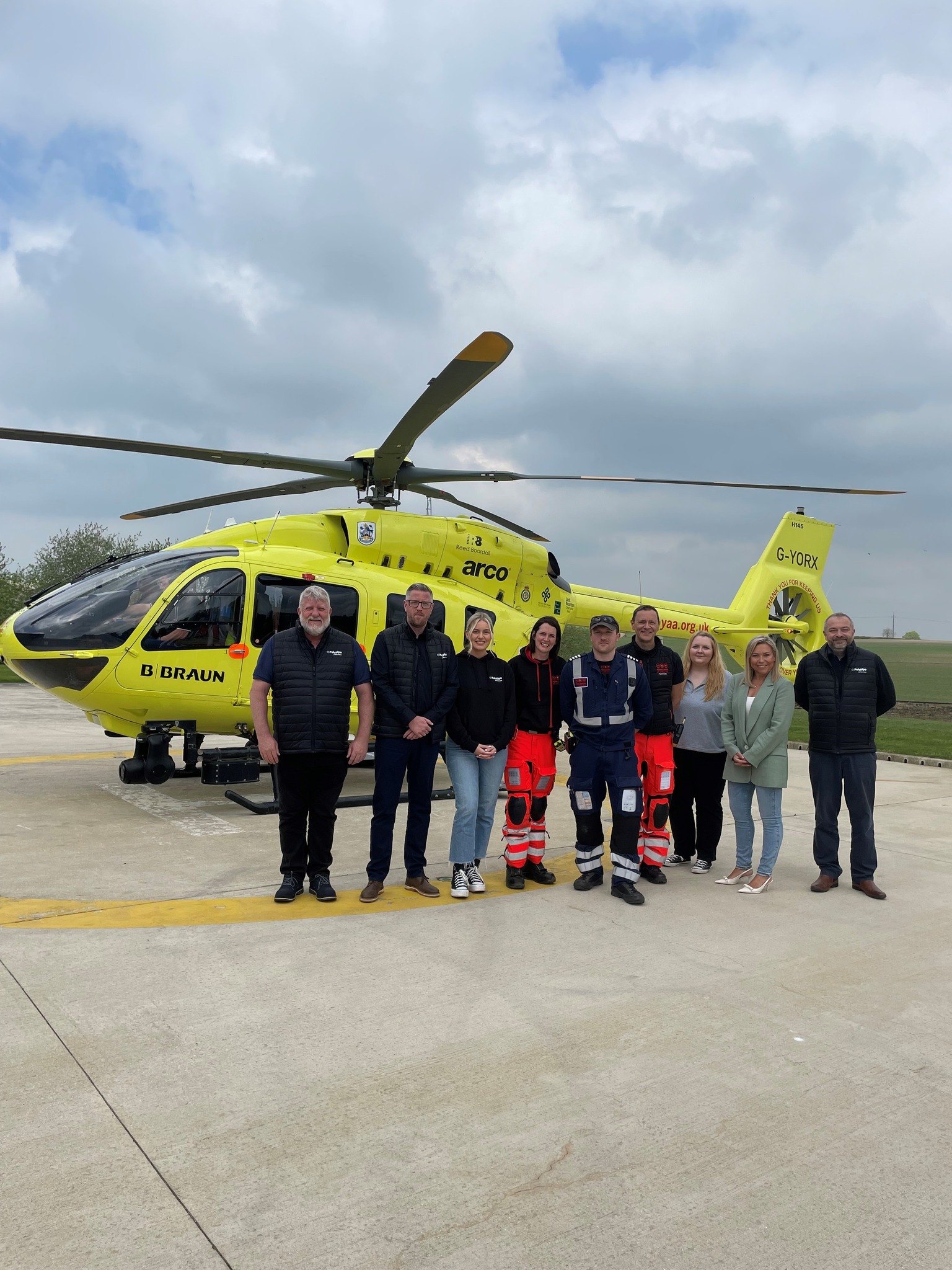 The team from Polypipe Building Products stand in front of a yellow helicopter which belongs to the charity, Yorkshire Air Ambulance