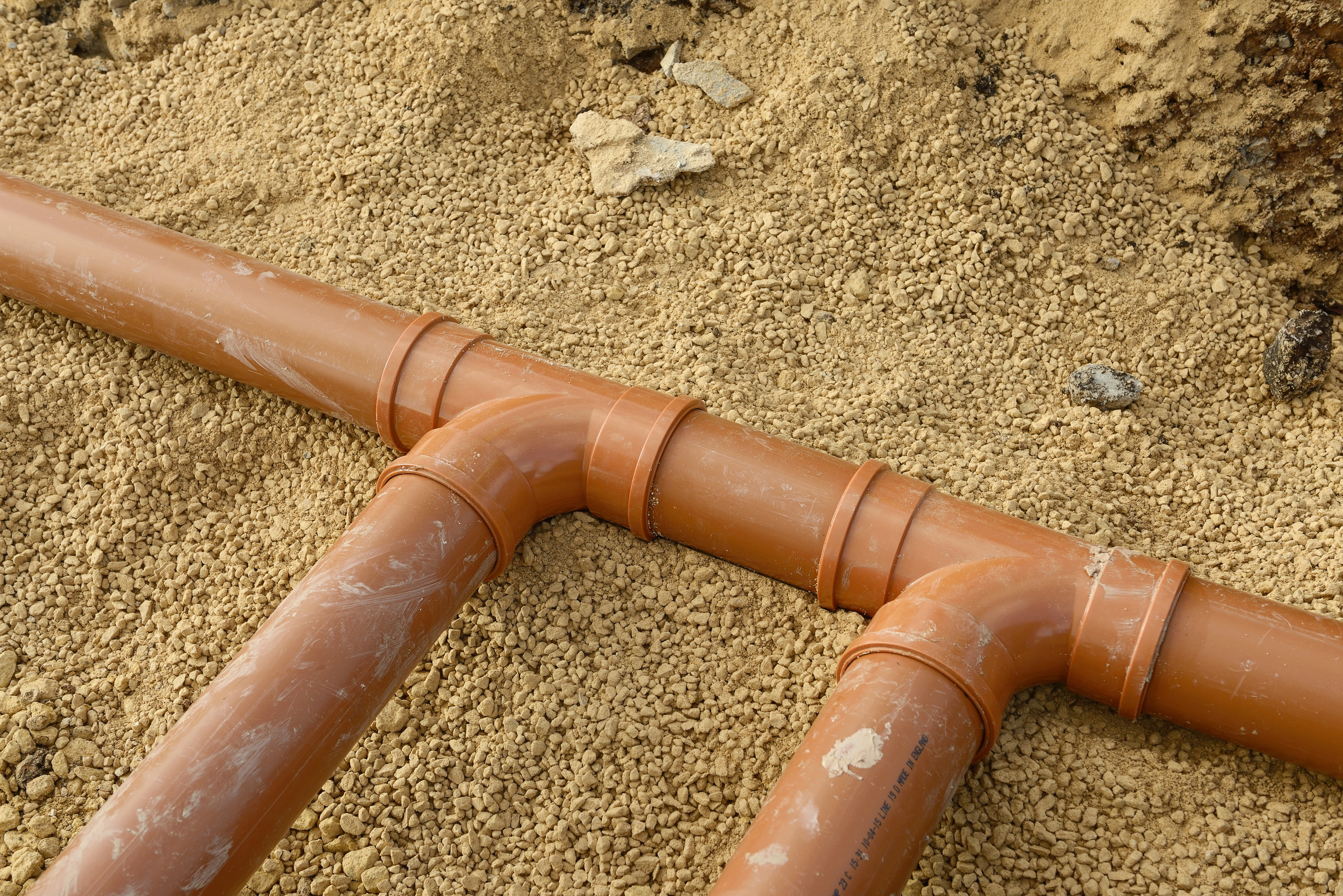 Below ground drainage pipes sat in a bed of sand in a trench on a building site.